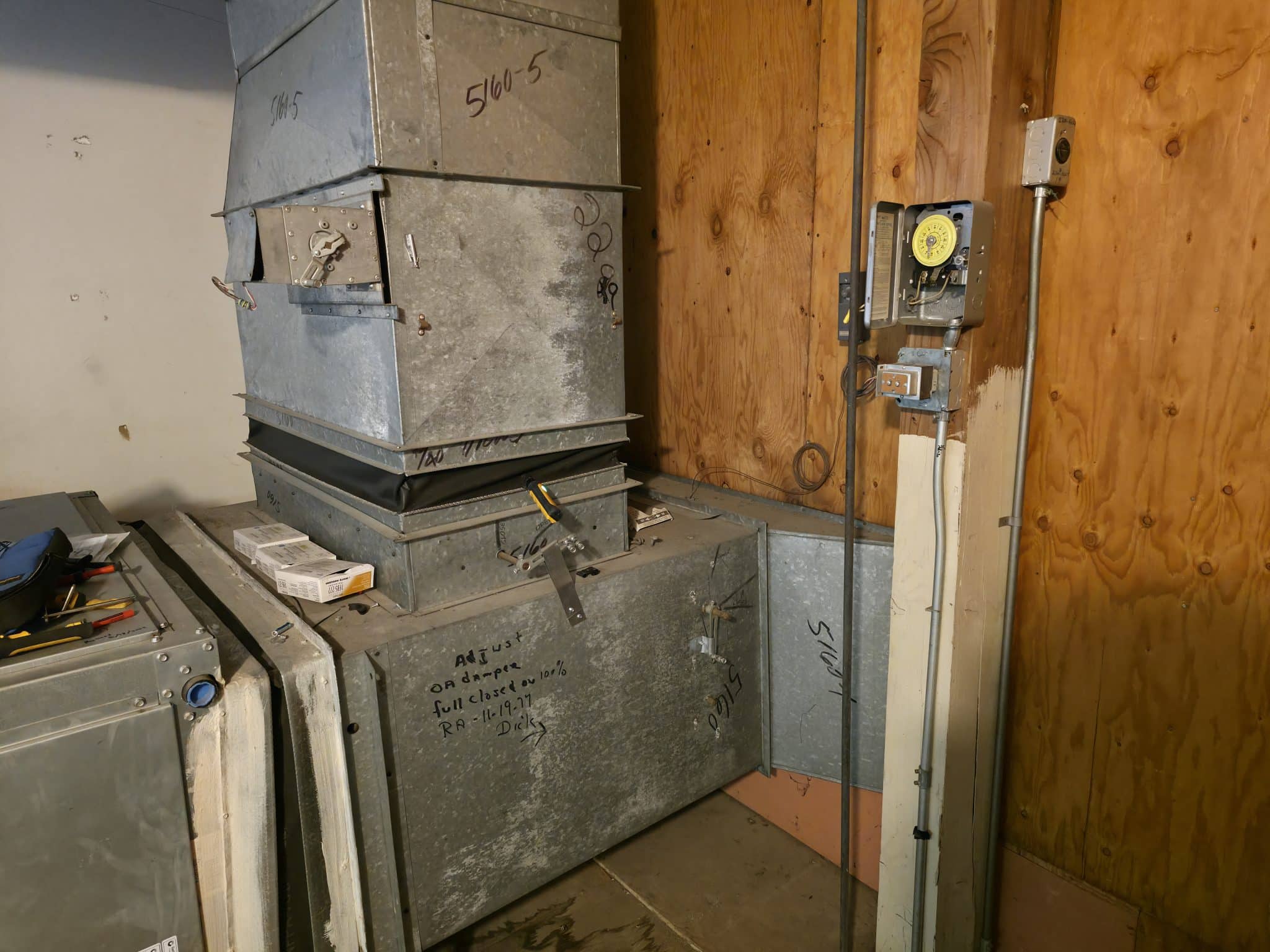 Vintage galvanized sheet metal ductwork plenum and manual time clock control during hvac system refurbishment in mountain view, ca. Original 1999 commissioning notes still visible on the damper housing.
